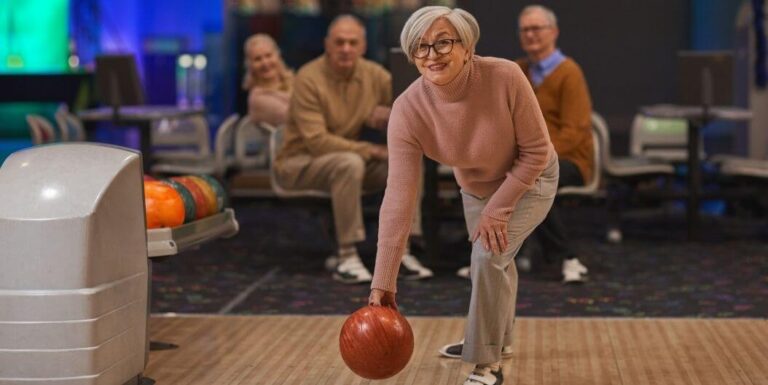 Elderly Woman Bowling with Friends Watching at Assisted Living Facility
